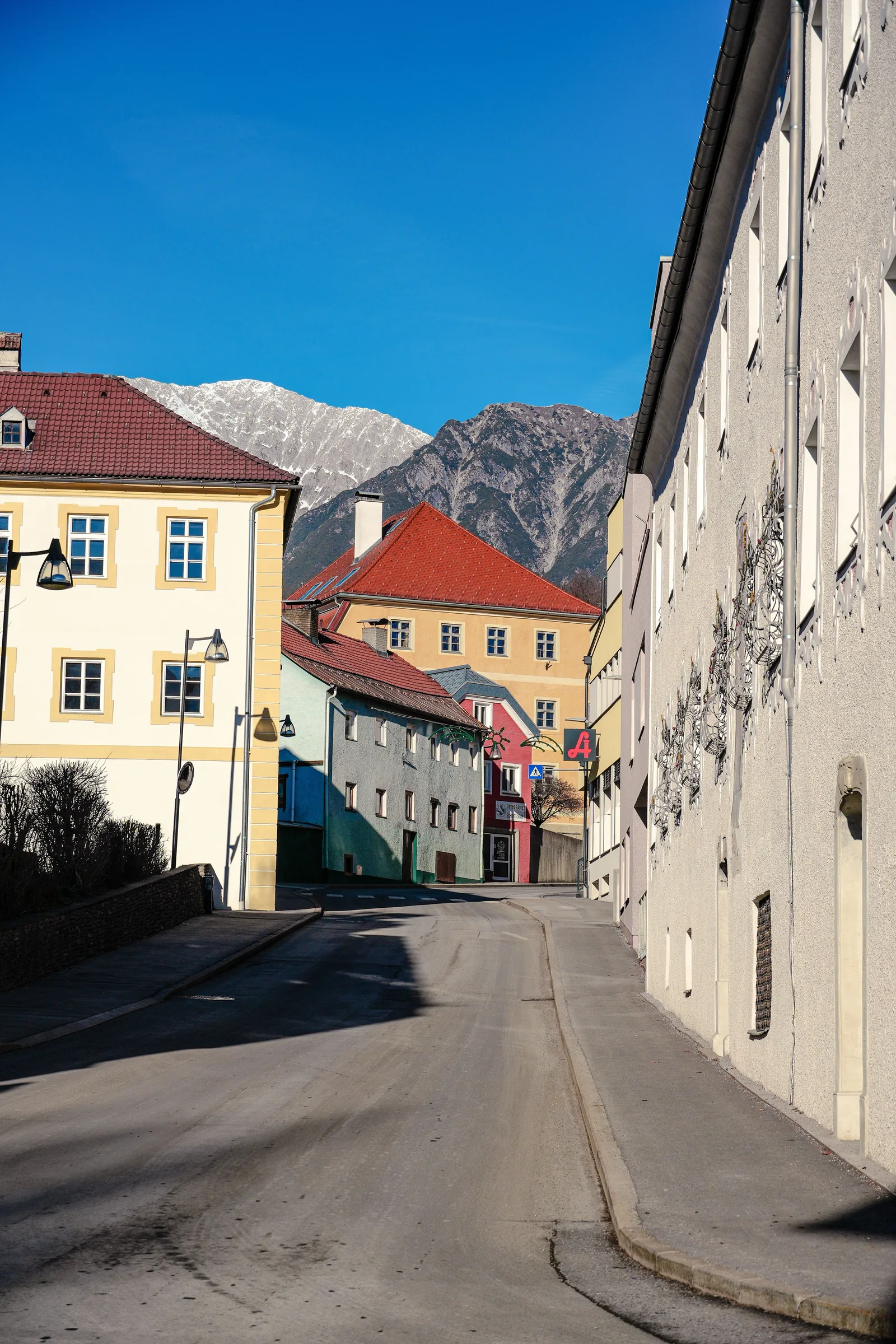 Helle Häuser entlang einer Straße im Tiroler Ortszentrum mit Bergen im Hintergrund